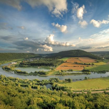Luchtfoto van het Altmühltal met een kronkelende rivier die een lus vormt rond groene velden en bossen onder een blauwe lucht met witte wolken.