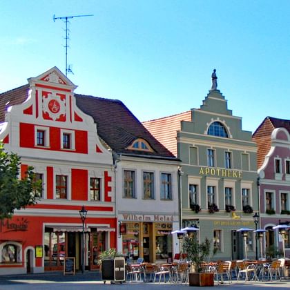 Kleurrijke historische gebouwen rond het marktplein van Cottbus met rood-witte gevels, café-terrassen en blauwe lucht.