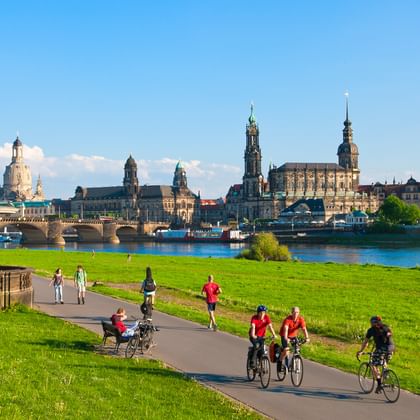 Fietsers op het Elbe fietspad met Dresden's historische skyline met de Frauenkirche en barokke architectuur over de rivier.