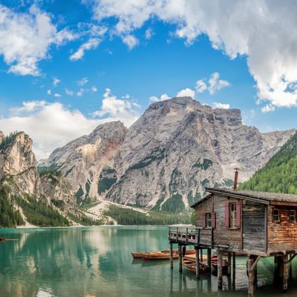Pragser Wildsee meer in de Dolomieten met turquoise water, houten boothuis op palen, kleine boten en dramatische bergtoppen.