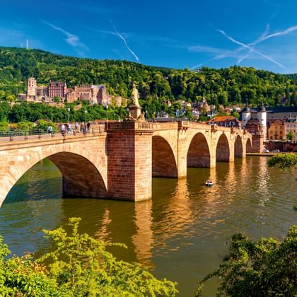 Heidelbergs Oude Brug met stenen bogen over de Neckar, met kasteelruïne op de heuvel en historische stadsgebouwen.