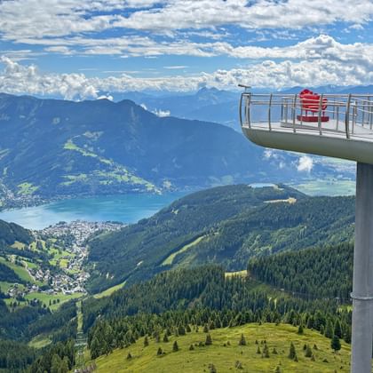 Verhoogd uitkijkplatform op Schmittenhöhe met bezoekers met uitzicht op het meer van Zell am See, groene bergen en valleien in de Kitzbüheler Alpen.