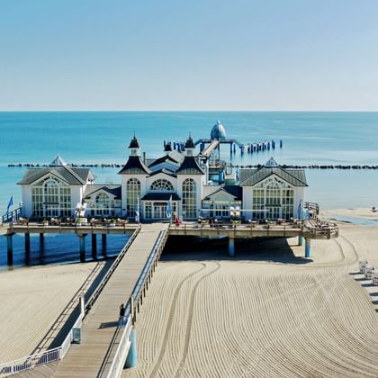 Wit sierlijk piergebouw met torens en koepels dat de Oostzee in reikt bij het strand van Sellin op Rügen, met zandstrand en blauw water.