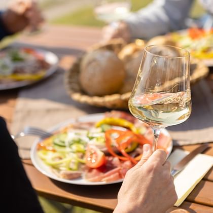 Hand houdt glas witte wijn boven houten tafel met traditionele Oostenrijkse vleeswaren, groenten en brood in de Wachau.