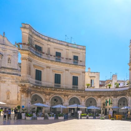 Piazza Plebiscito in Martina Franca met Basiliek San Martino, gebogen arcadecolonnade en terrasjes onder een heldere blauwe lucht.
