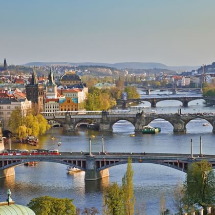 Panoramisch uitzicht op Praag met meerdere stenen bruggen over de Moldau, historische architectuur en rode pannendaken.