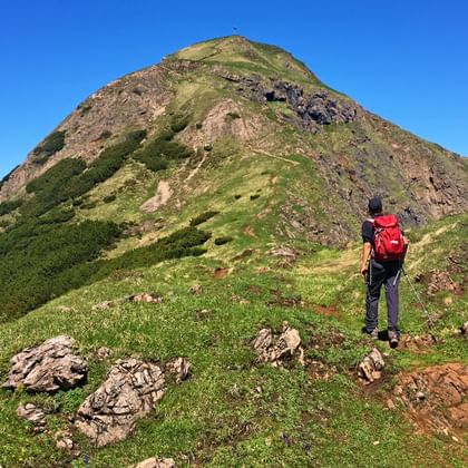 Wandelaar met rode rugzak op grasrijke bergkam richting Spielberghorn top onder blauwe hemel in de Oostenrijkse Alpen.