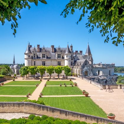 Renaissance-kasteel in Loire-vallei met formele tuinen, verzorgde gazons en riviergezicht onder blauwe hemel omlijst door groen gebladerte.