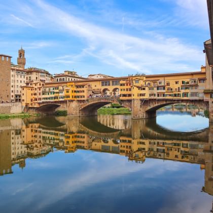 De beroemde Ponte Vecchio brug in Florence met zijn karakteristieke winkels gebouwd langs de zijkanten, over de Arno met perfecte reflecties.