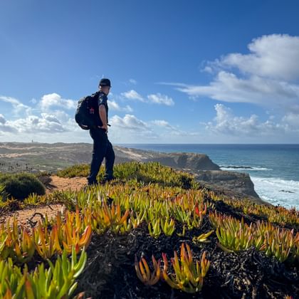 Wandelaar met rugzak op klif met kleurrijke vetplanten met uitzicht op de Atlantische Oceaan op de Rota Vicentina in Portugal.
