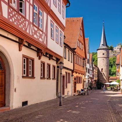 Smalle geplaveide straat in Karlstadt met traditionele vakwerkhuizen. Een middeleeuwse stenen toren met spitse torenspits rijst op de achtergrond.