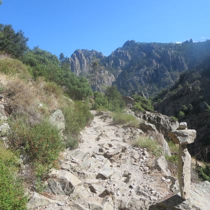 Rotsachtig wandelpad door de Tavignano-kloof op Corsica met dramatische granieten kliffen op de achtergrond onder een heldere blauwe lucht.