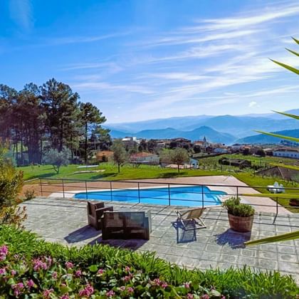 Zwembad bij Quinta Manhas Douro met stenen terras, loungemeubels en panoramisch uitzicht op bergen en wijngaarden in Provesende, Portugal.