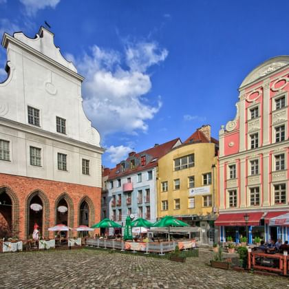 Kleurrijke historische gebouwen rond een geplaveide plein in Szczecin. Wit barok gebouw met bogen, roze sierlijke gevel en gele gebouwen.