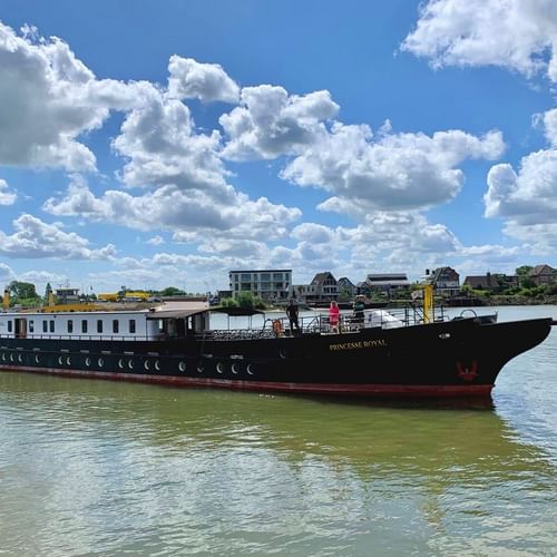 MS Princesse Royal, een zwart-wit riviercruiseschip met meerdere dekken en ramen, varend op kalm water onder bewolkte blauwe lucht.